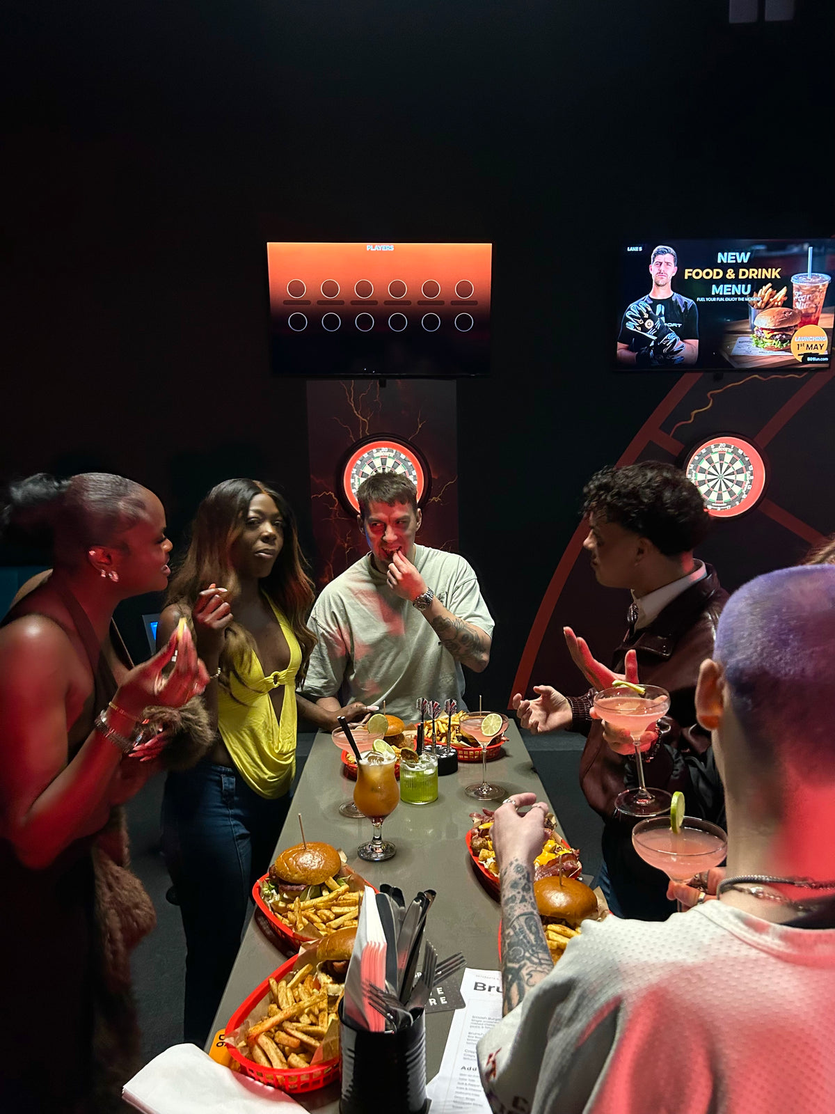 Group of people socializing around a table with food and drinks in a bar setting.